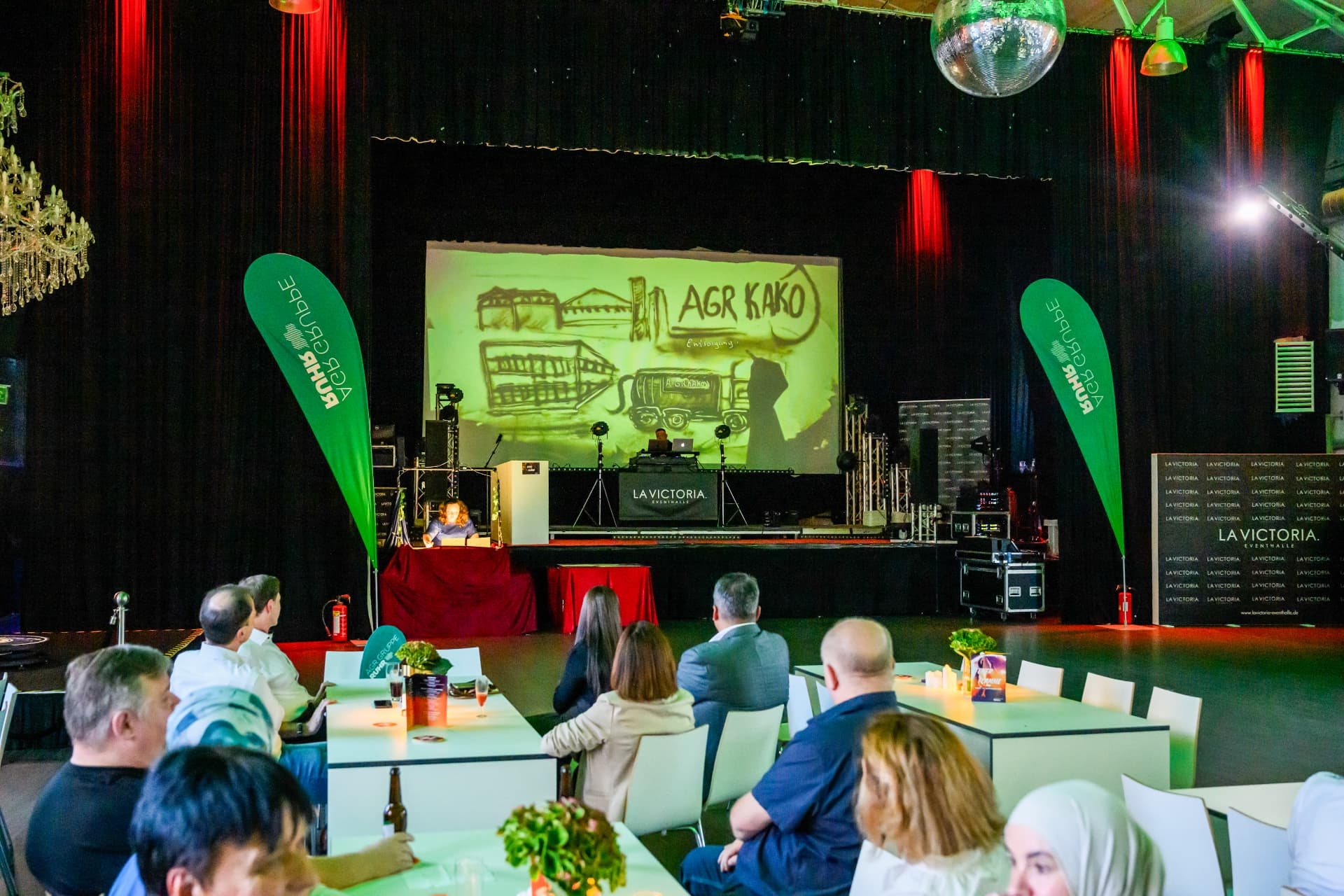 Festsaal mit Gästen und Sandshow-Projektion auf der Bühnenleinwand
